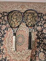 Pair of two Head tennis rackets on patterned rug; one racket has white grip, the other black grip showing wear