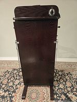 Full front view of the Arrow professional pants presser with dark mahogany wood panel, chrome side supports, and black and white control dial on top.