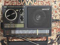 Top view of Retekess TR618 radio showing speaker, buttons, knobs, tuner scale, and carry handle folded flat.