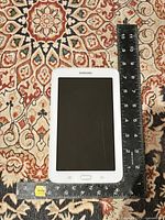 Front side of white Samsung Galaxy Tab with touchscreen displaying a black screen and a ruler measuring approximately 7 inches tall and 4.25 inches wide.