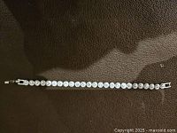 Full view of the silver plated tennis bracelet with round crystals on a dark background.