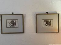 Two framed prints hanging on a textured wall, depicting Mayan or Aztec figures, with gold-colored frames and beige matting.