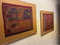 Photo showing both framed South American textile artworks mounted on a textured wall.