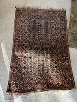 Full view of antique rug laid on carpet showing overall pattern and color