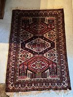 Full view of rectangular antique rug showing geometric and floral designs with fringed edges.
