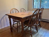 Full view of kitchen table with four spindle back chairs arranged around it, showing natural wood grain and turned legs.