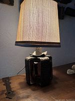 Front view of lamp illuminated, showing fabric shade and part of base with metal and glass details.