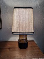 Front view of the lamp showing fabric shade lit and brown textured glass base on black metal stand.