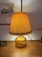 Front view of amber glass table lamp turned on on wooden surface with pleated shade.