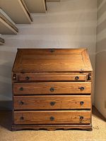 Front view of antique secretary desk closed, showing fold-down lid and three main drawers with round metal handles.
