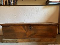 Front view of the wooden blanket chest showing the aged wood, flat lid, and keyhole latch.