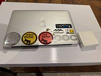 Closed Apple MacBook Air laptop showing stickers on the lid and the charger block placed on the side.