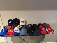 Array of assorted caps in various colors and embroidered logos, arranged on a table against a white wall.