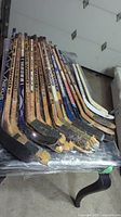 Photo showing the side view of multiple wooden Sher-Wood hockey sticks with taped blades and worn edges, arranged flat on a table.