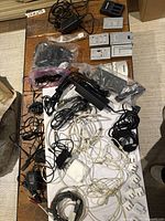 Top view of table with assorted cables and chargers, showing Apple power adapters, USB cables, and black power bricks.