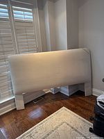 Full view of headboard leaning against wall and shutters, showing overall shape, color and legs