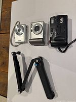 Three cameras and a GoPro extension stick on white background showing front and side angles