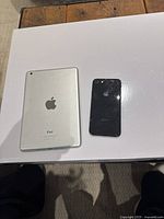 Top-down photo showing silver Apple iPad and black iPhone side-by-side on a white surface.