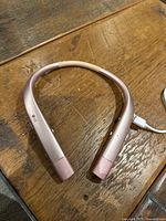 Rose gold LG Bluetooth headphones with neckband style shown charging and resting on wooden surface.