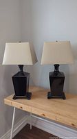 Two lamps side by side on wooden table against wall, front view