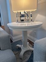 Front view of white round pedestal table with lamp on top