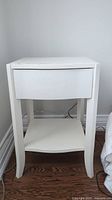Front view of white side table showing drawer and open shelf.