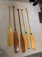 Overview of five wooden canoe paddles laid flat on floor