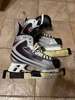 Side view of the Bauer Vapor XII hockey skates showing the color scheme, laces, and attached blade holders with protective covers.
