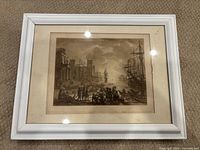 Framed print showing a harbor scene with ships, people, and buildings, capturing the full item with frame and matting.