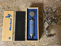 Overall lot showing Bluebird microphone in original wooden box with foam insert, silver shock mount, and microphone clip.