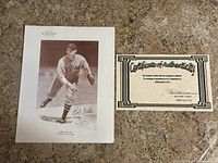 Two 8.5 x 11 inch signed images of Bob Feller baseball player and a certificate of authenticity shown on carpeted floor.