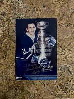 Front view of the autographed 4x6 color photo showing Bobby Baun in Toronto Maple Leafs uniform holding the Stanley Cup. Silver marker autograph and personalized message visible.