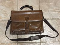 Brown leather Daniel briefcase closed showing front outer appearance including front pockets, top handle, and shoulder strap.
