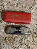 Hohner Golden Melody harmonica with closed red carrying case on granite surface