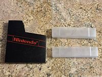 Two black Nintendo branded NES cartridge cases and four clear plastic SNES cartridge cases on a granite countertop.