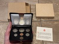 Photo showing the open black presentation case holding seven Canadian coins from 1975 with the informational card on the side, outer cardboard box visible.