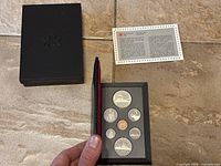 Open case showing seven proof coins arranged in black foam insert with certificate card and black outer case.