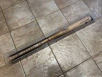 Full length of the bat in clear protective display case on tiled floor.