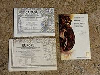 Three folded vintage maps of Canada, Europe, and Maine in their original covers with National Geographic branding.