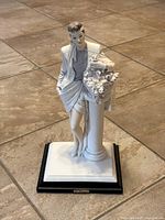 Full view of Vittorio Tessaro porcelain figurine showing woman leaning on floral column on tiled floor.