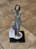 Front view of the porcelain figurine showing the woman in an off-shoulder long dress with floral bouquet and a card on the base.