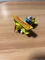 Angled side view of the yellow biplane toy with Smurf pilot on wooden surface.