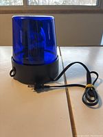 Blue strobe light resting on a table with a power cord coiled beside it, showing details of the translucent blue dome and black base