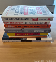 Stack of seven books showing spine titles on a wooden surface.