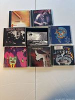 Top view of 8 music CD cases arranged in two rows, showing album covers of Ratatat LP3, Mighty Morphin Power Rangers The Movie, Cowboy Junkies, The Punisher, and others.