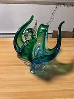 Angle showing the artistic green and blue glass bowl shaped like a duck with pointed extensions and clear glass feet.