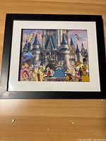 Full front view of the framed Disney character pin picture depicting multiple classic characters in front of a castle with a black frame and white mat.