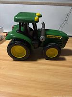 Side view of green John Deere toy tractor with large black tires and yellow wheel rims.