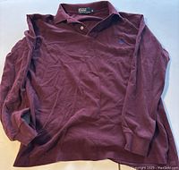 Full front view of maroon Polo Ralph Lauren long sleeve polo shirt laid flat showing button collar and long sleeves.