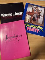 Three press kits/folders for films 'Wrong is Right', 'Bachelor Party', and 'Scandalous' arranged on wooden surface.